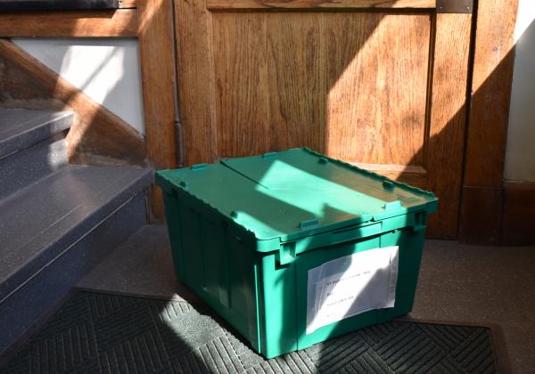 Closed green courier bin on the ground in front of a door and stairway